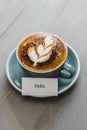 Cup of coffee with latte art and Hello greeting text on wood table