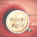 Cup of coffee latte, cappuccino on a pink wood table. Words welcome world written on a coffee top.