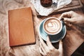 Cup of coffee latte and red book on wooden table or background in woman hands from above Royalty Free Stock Photo