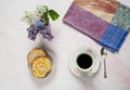 A cup of coffee, lilac flowers Syringa vulgaris and a sweet homemade turmeric bun on a pastel pink marble background.