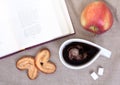 Cup coffee on linen tablecloths with pieces of sugar, cookies, red apple and an open book, top view