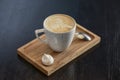 Cup of coffee on the little board over black background. Latte art. Little coffee mug and spoon.