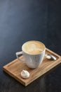 Cup of coffee on the little board over black background. Latte art. Little coffee mug and spoon.