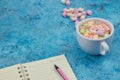 Cup with coffee and marshmallows, blank open notebook with pen on abstract blue background. Top view. Flat mockup. space for text Royalty Free Stock Photo