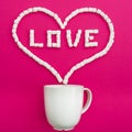 Cup of coffee and marshmallows on pink background. Heart symbol and quote Love. Flat lay. Top view Royalty Free Stock Photo