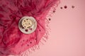 Cup of coffee with marshmallows, plaid, dried rose petals on a light pink background.