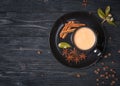 Cup of coffee with milk. Black cappuccino mug with plate decorated anise and cinnamon sticks. Coffee beans. Dark natural wooden ta