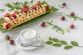 Cup of coffee with milk, cake with strawberry, ripe cherry berries and fresh flowers on the light table. Summer romantic breakfast Royalty Free Stock Photo