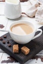 A Cup of coffee with milk and cubes of cane sugar on a wooden stand. Background of white rustic boards. Copy space