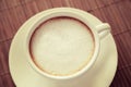 Cup of coffee with milk foam on wooden table seen from top.