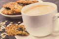 Cup of coffee with milk and fresh baked oatmeal cookies with honey and healthy seeds on white plate. Delicious crunchy dessert Royalty Free Stock Photo