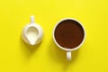 A cup with coffee and a milk jug on a yellow background, top view Royalty Free Stock Photo