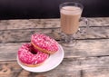 A cup of coffee with milk and two pink donuts standing on wooden textured background Royalty Free Stock Photo