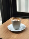 A cup of coffee on a minimal wooden table placed by a large glass window