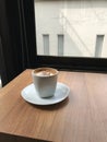 A cup of coffee on a minimal wooden table placed by a large glass window