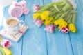 A cup of coffee on a notebook on a blue wooden background. Bright colors. Bouquet of flowers yellow and pink. The pink clock is Royalty Free Stock Photo