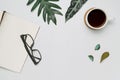 Cup of coffee and notebook with glasses on white wooden background with tropical monstera leaves. Royalty Free Stock Photo