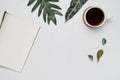 Cup of coffee and notebook on white wooden background with tropical monstera leaves. Royalty Free Stock Photo