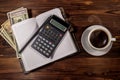 Cup of coffee and notepad with dollars, pencil and calculator on wooden desk. Top view. Financial concept Royalty Free Stock Photo