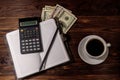 Cup of coffee and notepad with dollars, pencil and calculator on wooden desk. Top view. Financial concept Royalty Free Stock Photo