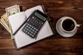 Cup of coffee and notepad with dollars, pencil and calculator on wooden desk. Top view. Financial concept Royalty Free Stock Photo