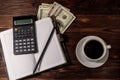 Cup of coffee and notepad with dollars, pencil and calculator on wooden desk. Top view. Financial concept Royalty Free Stock Photo