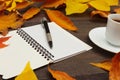 Cup of coffee, open notebook and pen among autumn fallen leaves on wooden background Royalty Free Stock Photo