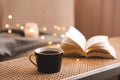 Cup of coffee with open paper book on rattan table in bedroom indoors close up over scented candle. Royalty Free Stock Photo
