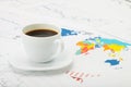 Cup of coffee over world map and financial documents