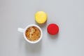 Cup of coffee and pair of colorful macarons or macaroons on gray background, top view