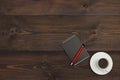 Cup of coffee, pen and black notebook on wooden desktop. View from above.