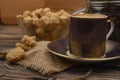 A Cup of coffee, pieces of brown sugar in a sugar bowl, coffee beans in a glass jar on a wooden background