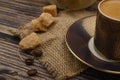 A Cup of coffee, pieces of brown sugar in a sugar bowl, coffee beans on a wooden background. Close up