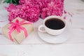 A cup of coffee, pink peonies pattern and gift box on wooden background