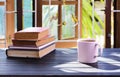 A cup of coffee is placed on the table by the window. with a pile of books and the morning sun shines in Royalty Free Stock Photo