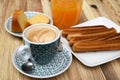 Cup of coffee with a plate of churros and a glass of orange juice