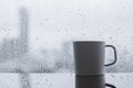 A cup of coffee puts on table in morning with rain drop on window.