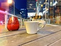 Cup of coffee and red glass cup candle on table top in night city  cafe  , modern buildings and traffic at street blurred night li Royalty Free Stock Photo