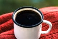 A cup of coffee on a red sweater. Metal cup in the morning on the nature. Spring mood, love and romance