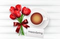 Cup of coffee with red tulips and red ribbon on a white wooden background Royalty Free Stock Photo