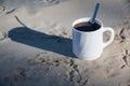 A cup of coffee on the sand. Bird footprints in the sand and a cup of white coffee with black coffee in the light of dawn. Royalty Free Stock Photo