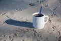 A cup of coffee on the sand. Bird footprints in the sand and a cup of white coffee with black coffee in the light of dawn. Royalty Free Stock Photo