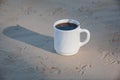 A cup of coffee on the sand. Bird footprints in the sand and a cup of white coffee with black coffee in the light of dawn. Royalty Free Stock Photo
