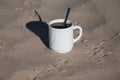 A cup of coffee on the sand. Bird footprints in the sand and a cup of white coffee with black coffee in the light of dawn. Royalty Free Stock Photo