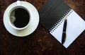 A cup of coffee on a saucer, next to a notebook with a pen. Work begins with breakfast. Royalty Free Stock Photo