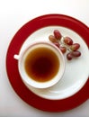 A cup of coffee set on a red-rimmed white plate with a few red grapes