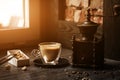 Cup of coffee in coffee shop vintage color. Coffee grinder and Brown cane sugar on wooden table with flare blurred