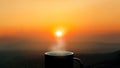 A cup of coffee with smoke on wood with sunrise landscapes background.