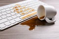 Cup of coffee spilled over computer keyboard on table Royalty Free Stock Photo