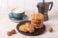 Cup of coffee, stack of oatmeal cookies, coffee maker on white wooden background Homemade bakery